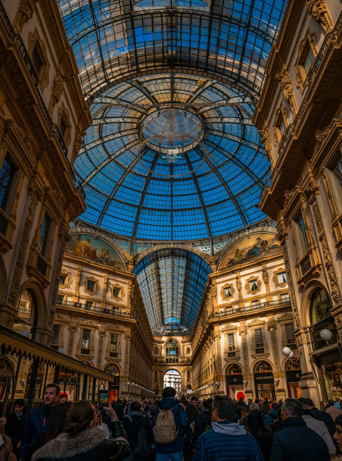 A grand glass-domed shopping arcade filled with people