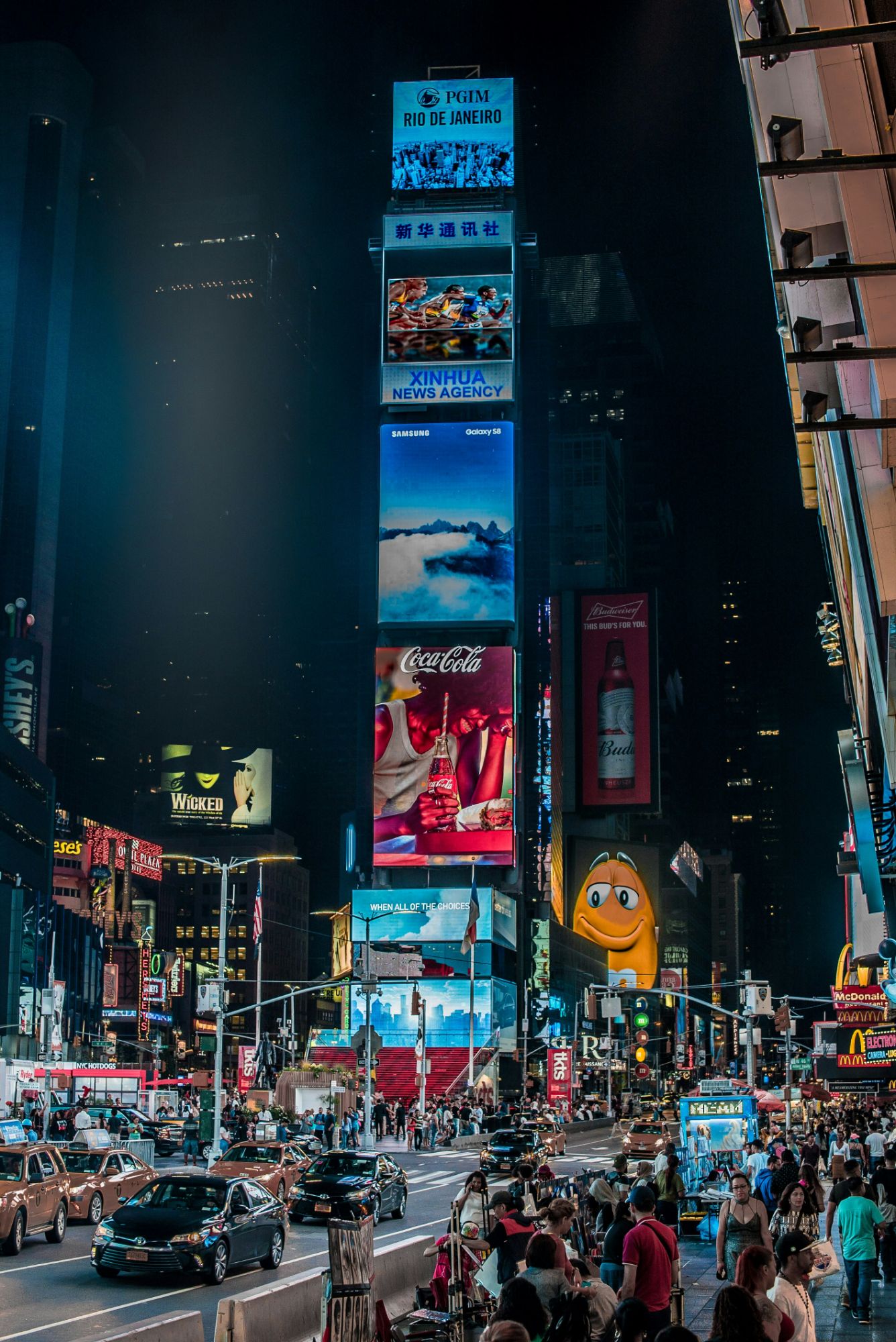 A glowing Coca-Cola billboard above a busy city street at night