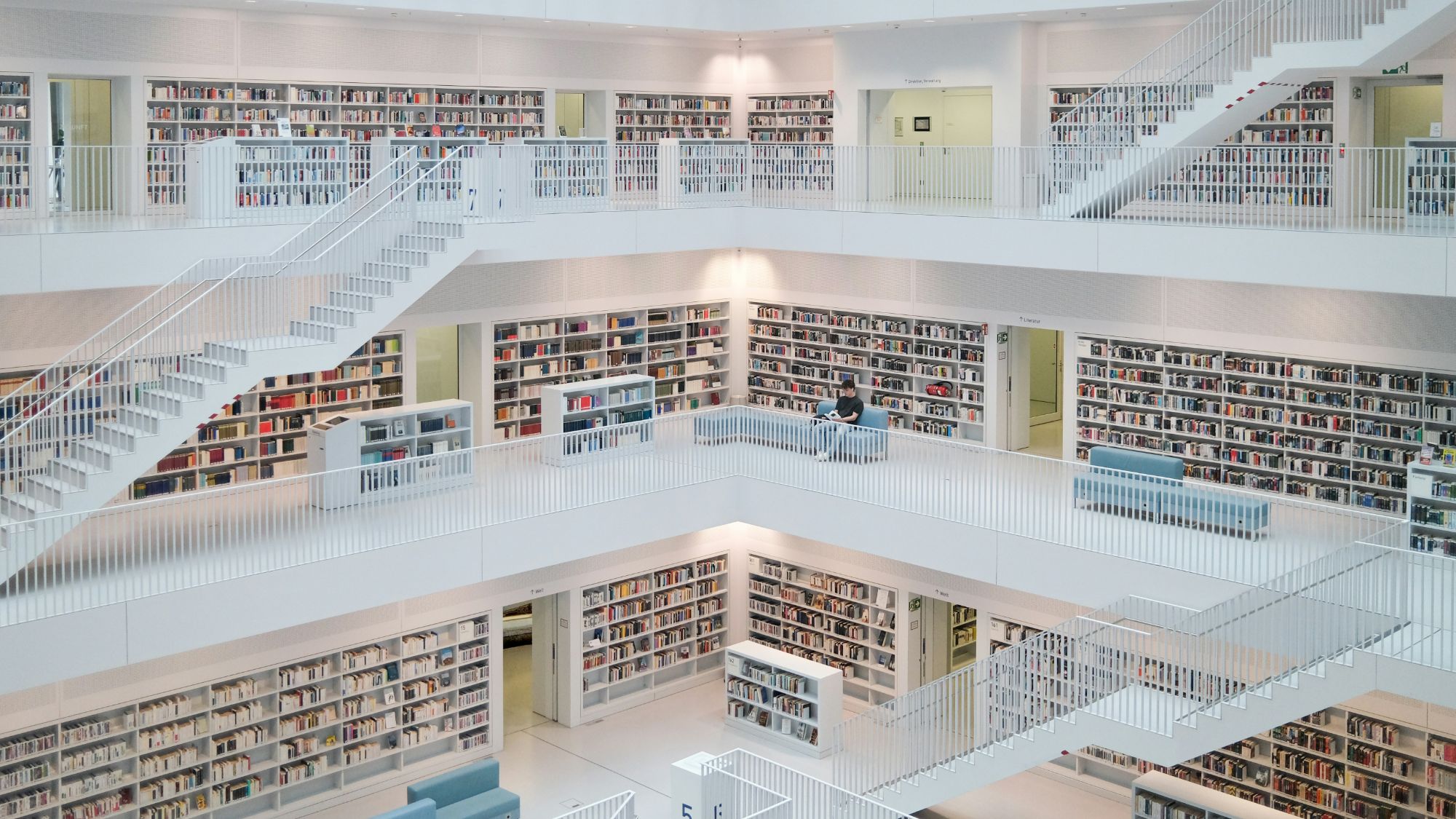 A multi-level library with white shelving stacked full of books