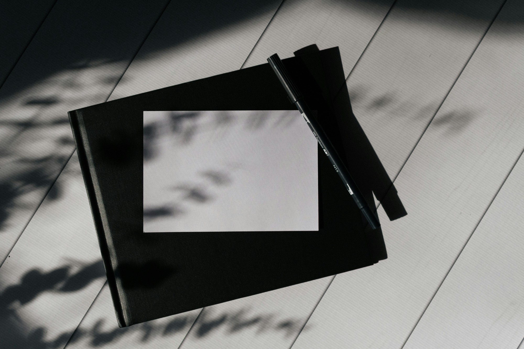 A blank white notebook page and a pen catching sunlight on a wooden surface